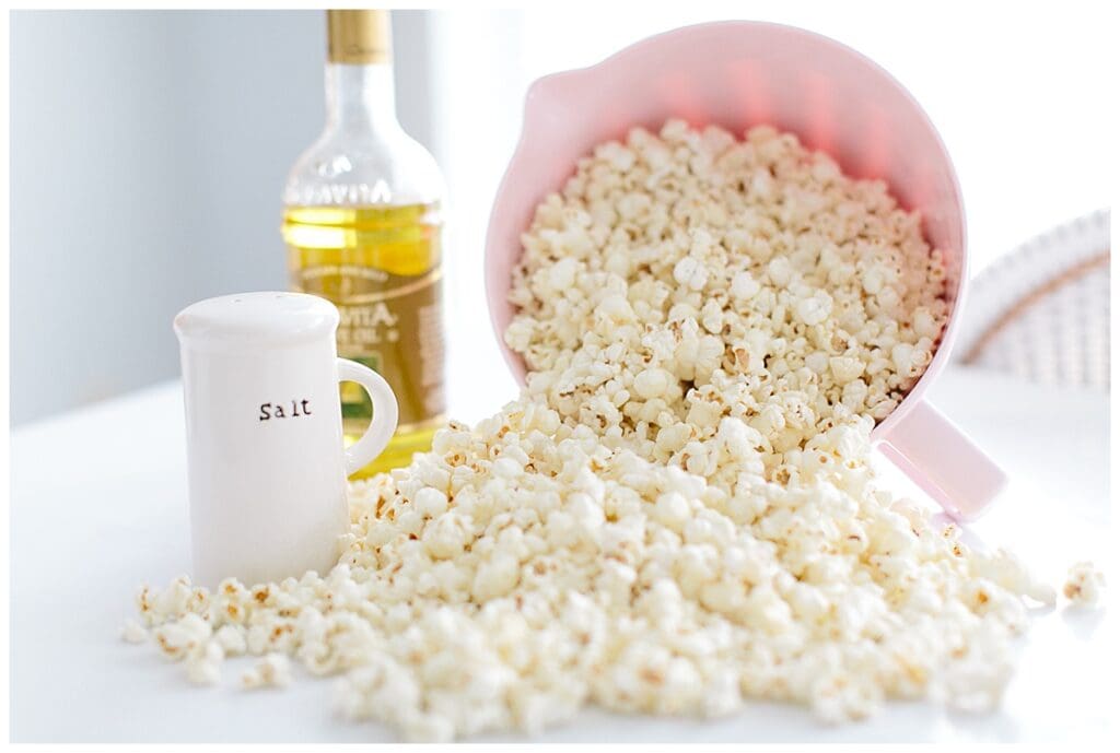 DIY popcorn bar - a pink bowl of popcorn tilted on its side next to salt and oil to use for toppings 